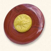 Ein Trauerknopf aus Jaspis mit einem gelben Knopf eines geliebten Menschen darauf. Der rote Jaspis ist oft geädert.
